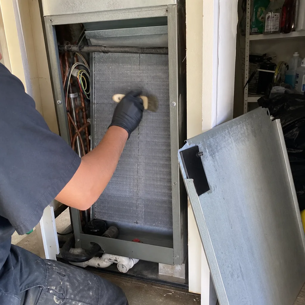 HVAC technician cleaning evaporator coils with a brush for system maintenance